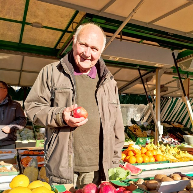 Hans Günther Kaufmann steht am Marktstand mit Apfel in der Hand, © Kulturamt der Stadt Miesbach