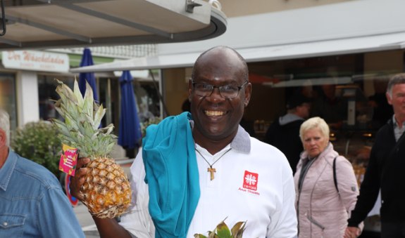 Pater Primus am Marktstand mit einer Ananas in der Hand, © Hartmut Wolf Pater Primus am Marktstand mit einer Ananas in der Hand, © Hartmut Wolf