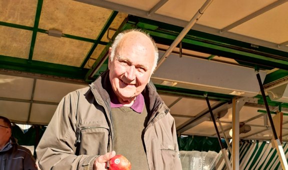 Hans Günther Kaufmann steht am Marktstand mit Apfel in der Hand, © Kulturamt der Stadt Miesbach Hans Günther Kaufmann steht am Marktstand mit Apfel in der Hand, © Kulturamt der Stadt Miesbach